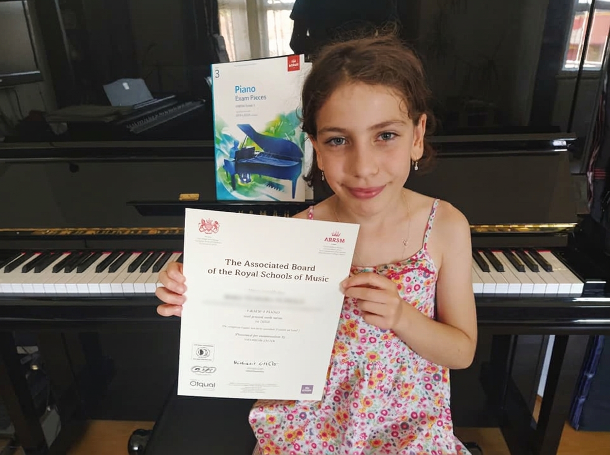 A young piano student at the piano, proudly holding her examination certificate